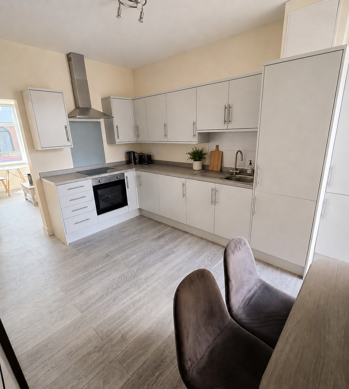 Shared fitted kitchen with dining chairs and a view into the communal lounge.